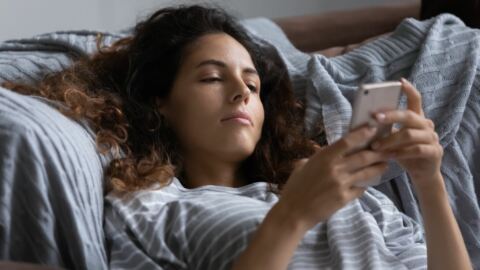 Bored female shopper laying in bed and browsing on her iPhone